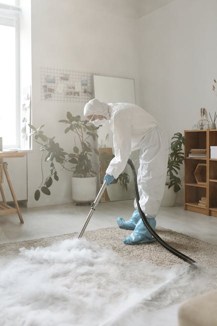 A professional cleaning specialist from Wood Green Carpet Cleaners is engaged in deep cleaning a residential carpet. The technician is dressed in a full white protective suit, including a hood, mask,